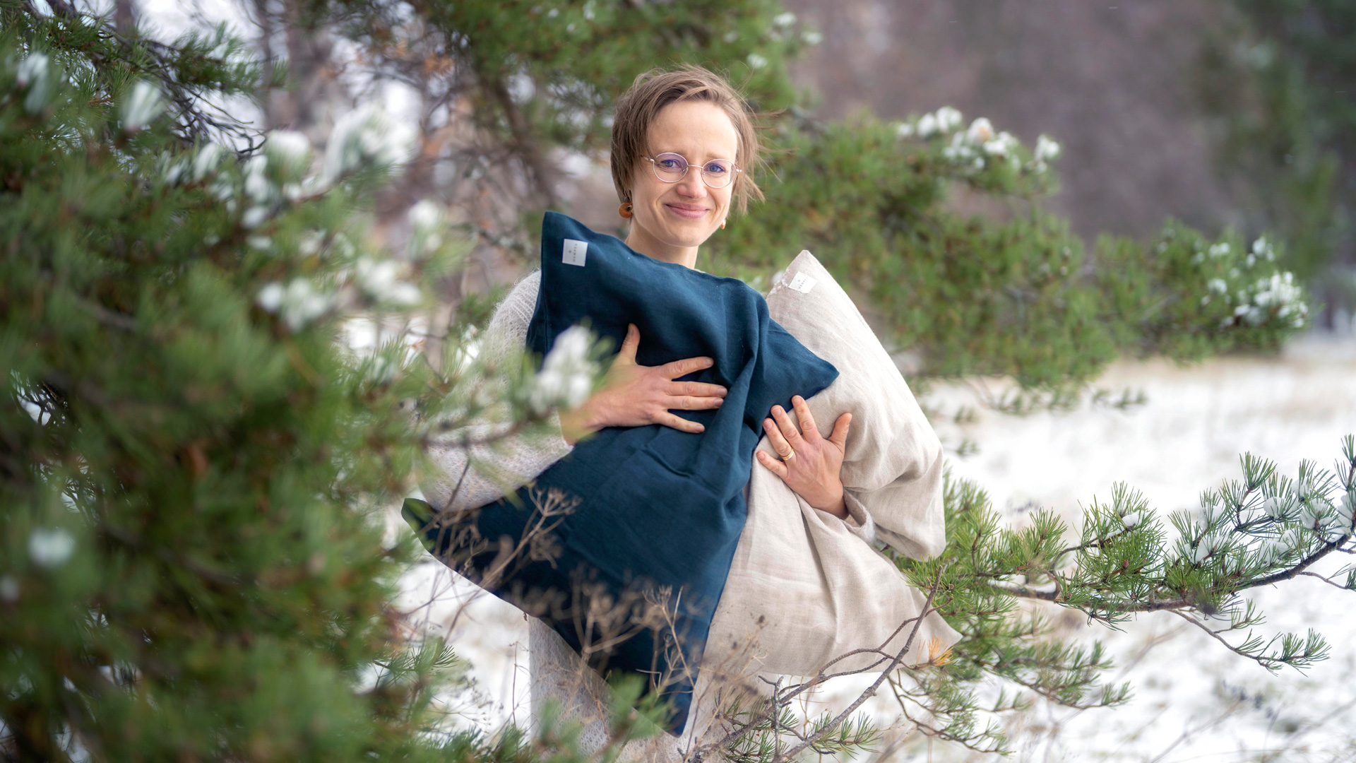 Marja-Maija Valtonen pitelee käsissään kahta pehmeään tyynyä talvisen puun katveessa